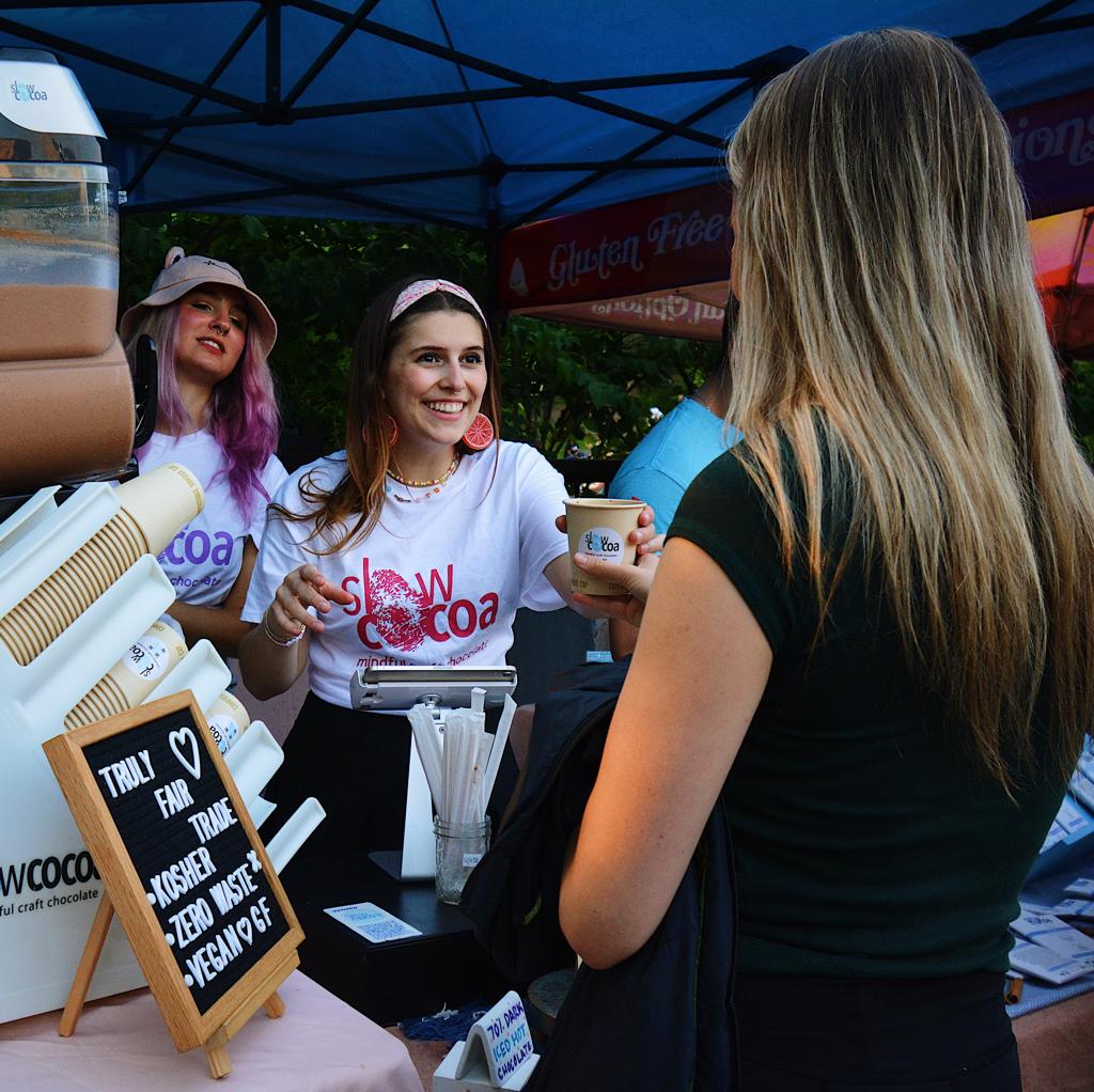 Woman in a white t-shirt with 'Show Cocoa' branding interacting with another woman at an outdoor event.
