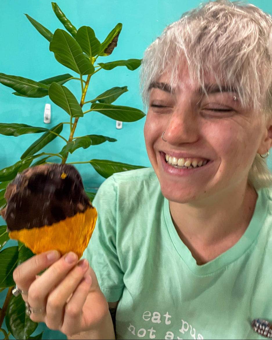 Smiling person holding a chocolate-dipped mango with a plant in the background