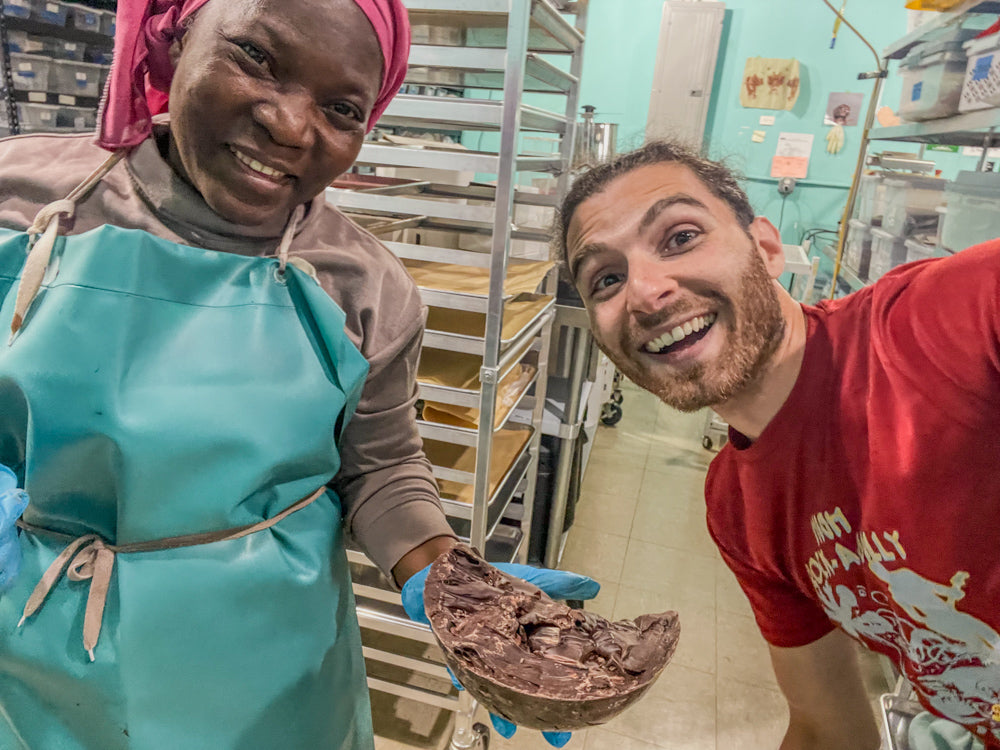 Two people in a kitchen, one holding a large piece of chocolate.