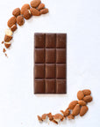 Chocolate bar with almonds arranged around it on a white background