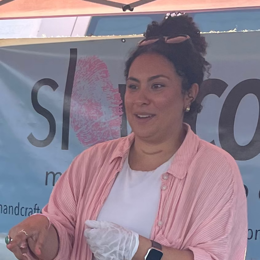 smiling woman standing outdoors with a food service gloved hand in front of a teal slowcocoa banner
