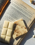 slowcocoa white chocolate with cinnamon is placed on an open book, page 53 of "The Age of Innocence", with pencil highlights and a cinnamon stick at the center binding of the book as though it's a bookmark.