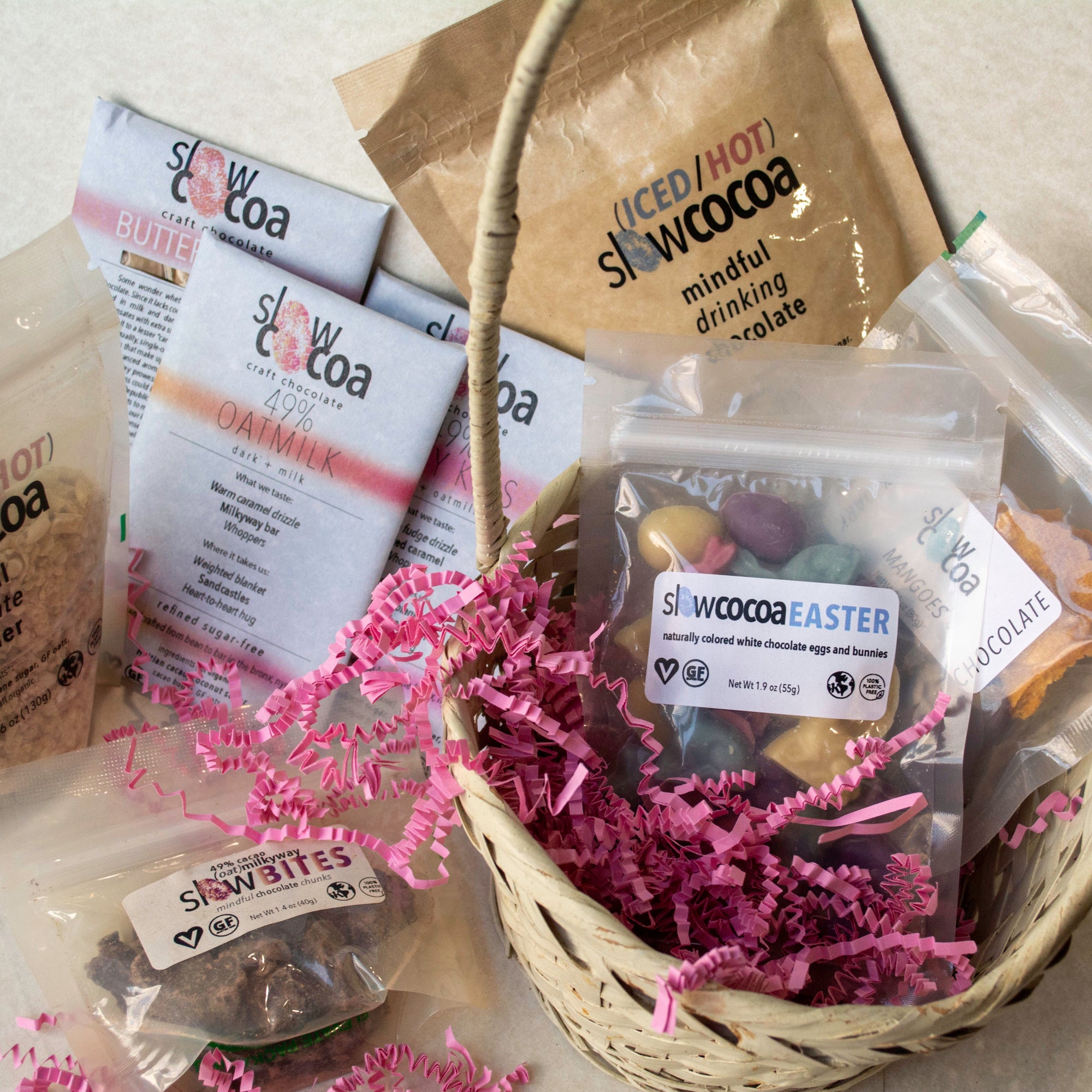 Basket with slowcocoa craft chocolate products including hot cocoa packets and a Easter-themed package on a textured surface.