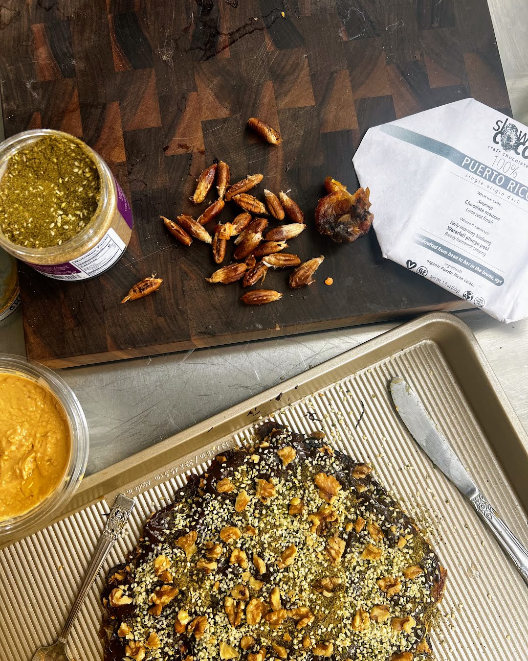 slowcocoa 100% Puerto Rico single-origin dark chocolate wrapper on a platter beside fresh-pitted dates, nut paste and a no-bake dessert served with fork and knife