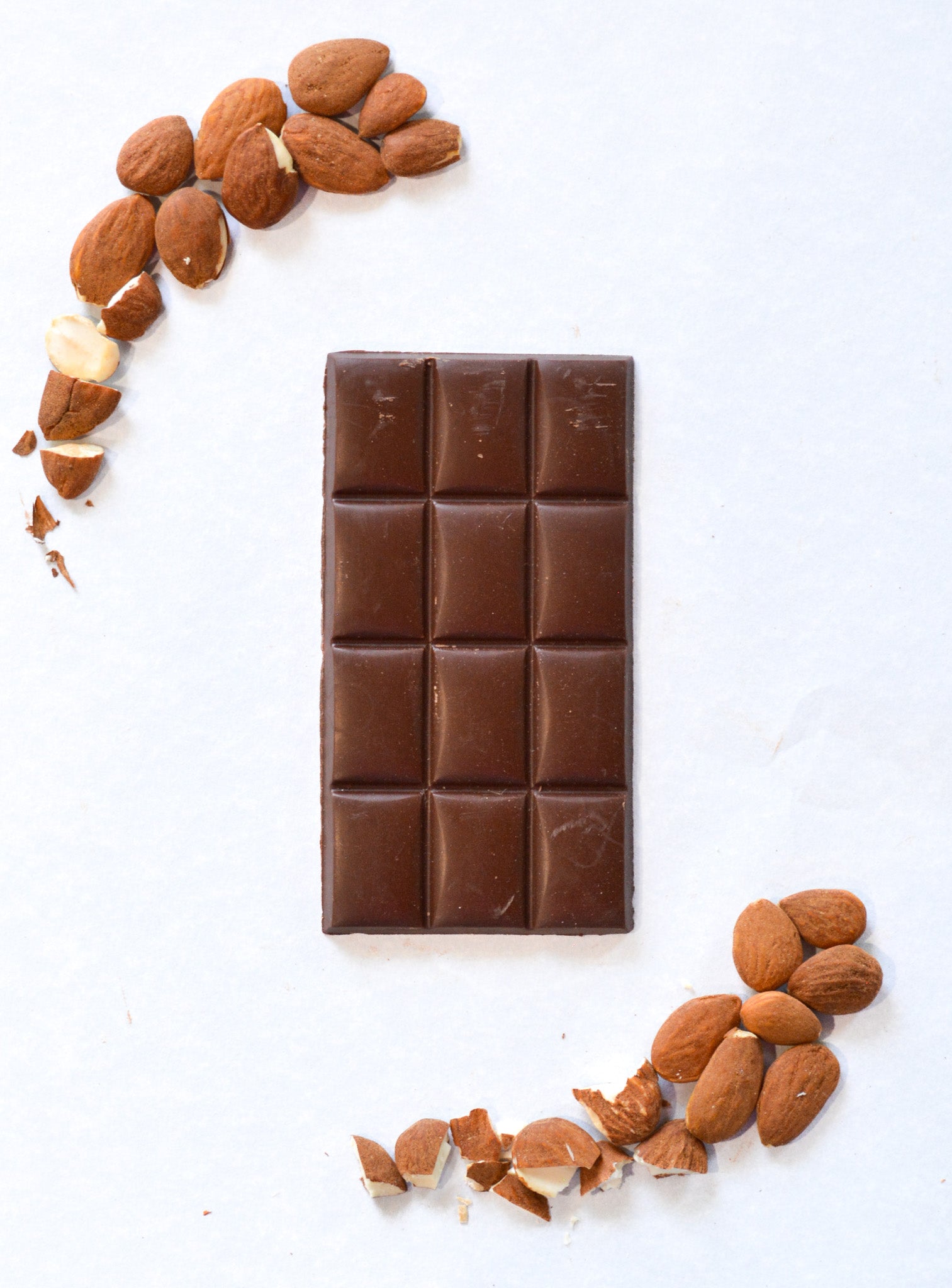 Chocolate bar with almonds arranged around it on a white background